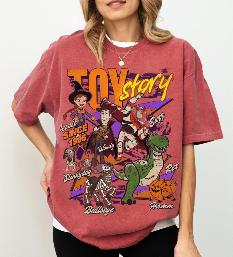 May include: Red-orange t-shirt featuring a graphic of Toy Story characters including Woody, Buzz Lightyear, and Rex. The shirt has the text "Toy Story" and "Jessie Since 1995".