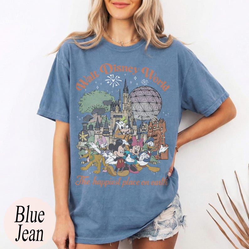 May include: Blue jean t-shirt with a Walt Disney World graphic. The design features the park's logo, iconic landmarks, and cartoon characters. The text "The happiest place on earth" is also included in the design.