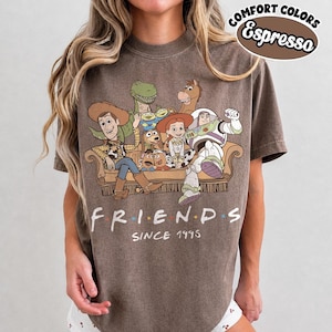 May include: An espresso-colored t-shirt featuring a graphic of Toy Story characters sitting on a couch with the text "FRIENDS SINCE 1995" below. The top right corner includes a circular logo with the text "COMFORT COLORS Espresso".