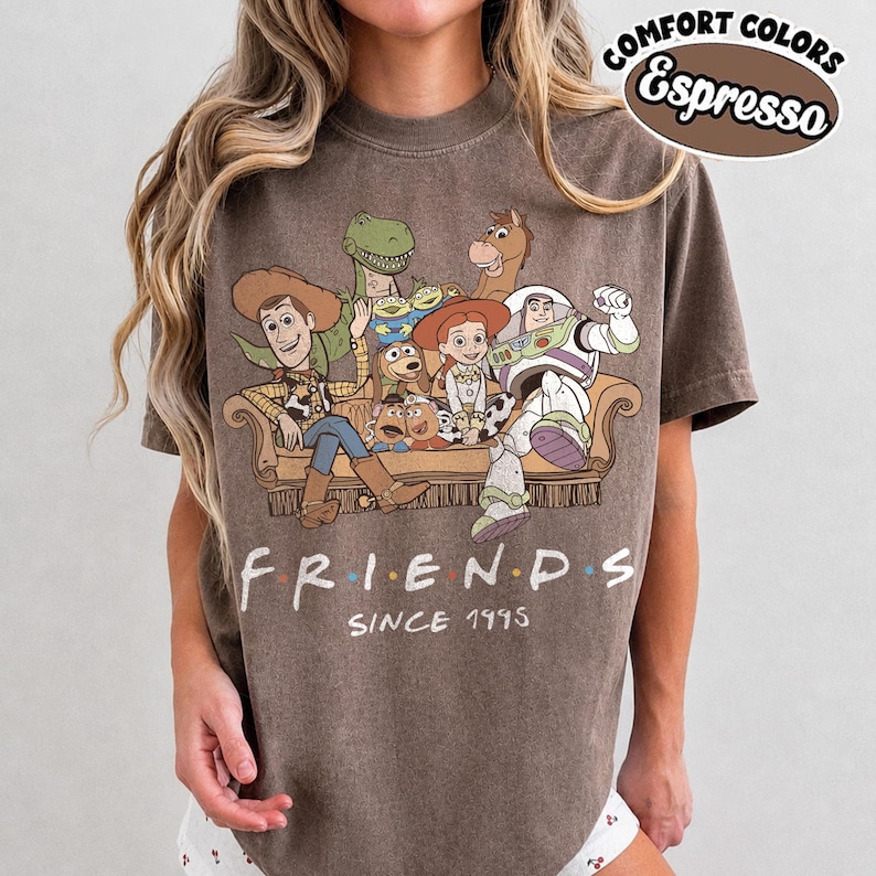 May include: An espresso-colored t-shirt featuring a graphic of Toy Story characters sitting on a couch with the text "FRIENDS SINCE 1995" below. The top right corner includes a circular logo with the text "COMFORT COLORS Espresso".