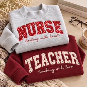 May include: A light gray sweatshirt with red polka dot applique letters spelling NURSE and the text healing with heart, layered over a maroon sweatshirt with cream polka dot letters spelling TEACHER and the text teaching with love.