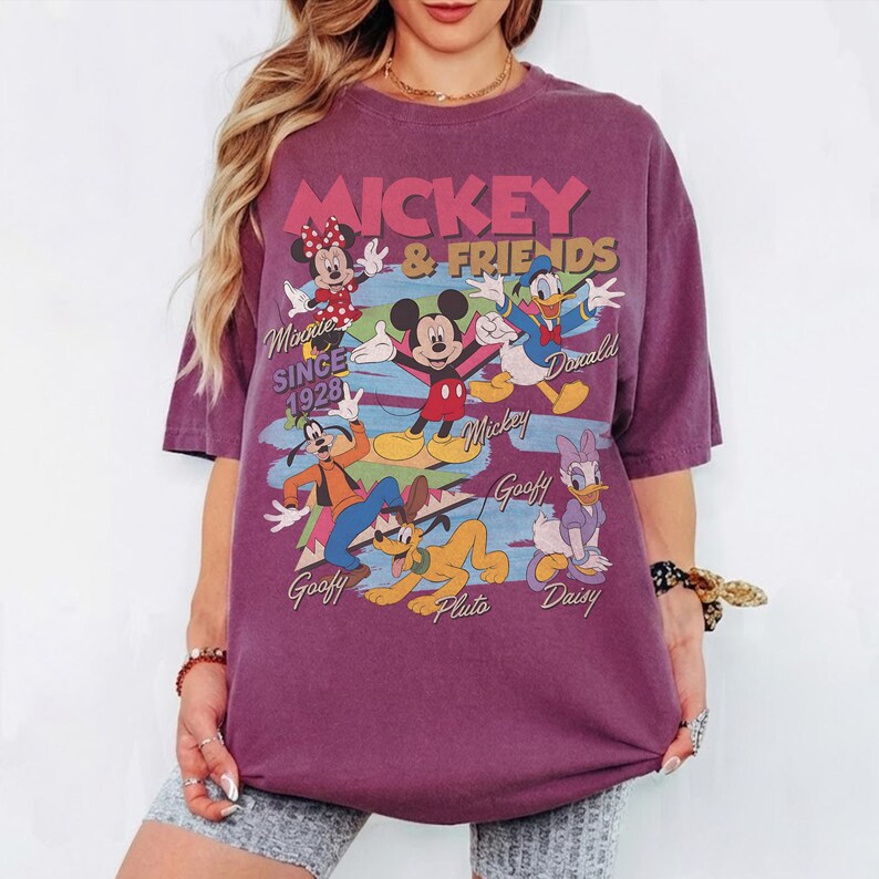 Peut inclure: T-shirt violet avec l'inscription "Mickey & Friends" et les personnages de dessins anim&eacute;s Mickey Mouse, Minnie Mouse, Donald Duck, Dingo, Pluto et Daisy Duck. Le t-shirt comprend &eacute;galement le texte "Since 1928".