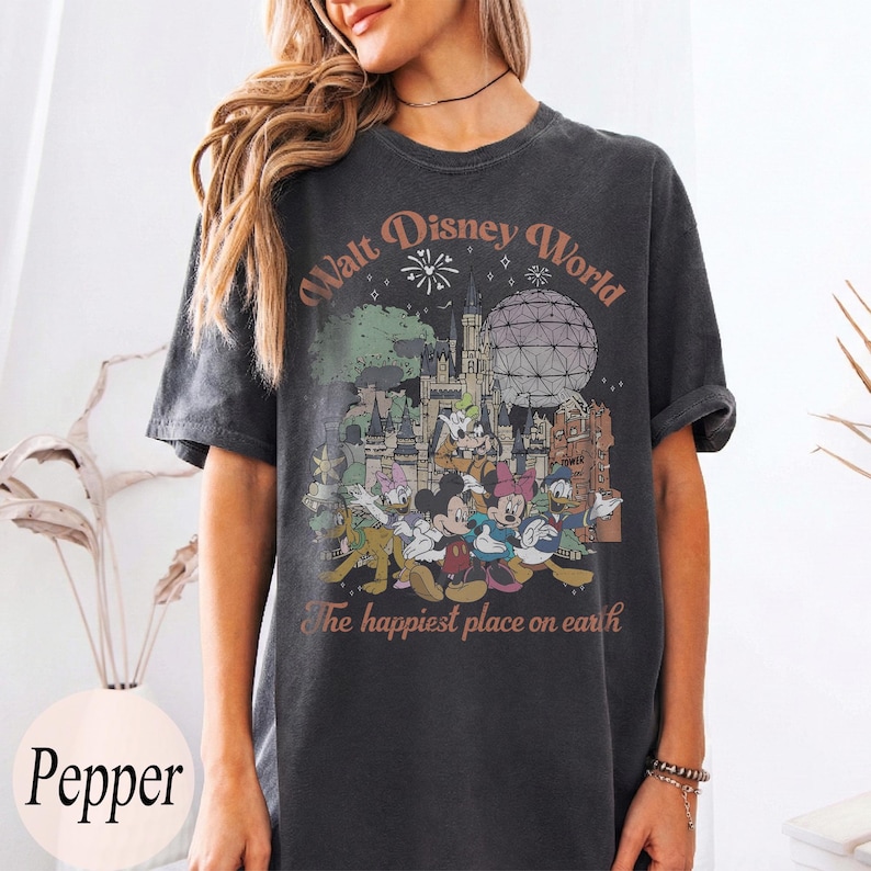 May include: Dark gray t-shirt featuring a colorful graphic of Disney characters and landmarks, including Mickey Mouse, Minnie Mouse, and Cinderella's castle. The text "Walt Disney World" and "The happiest place on earth" are printed on the shirt.