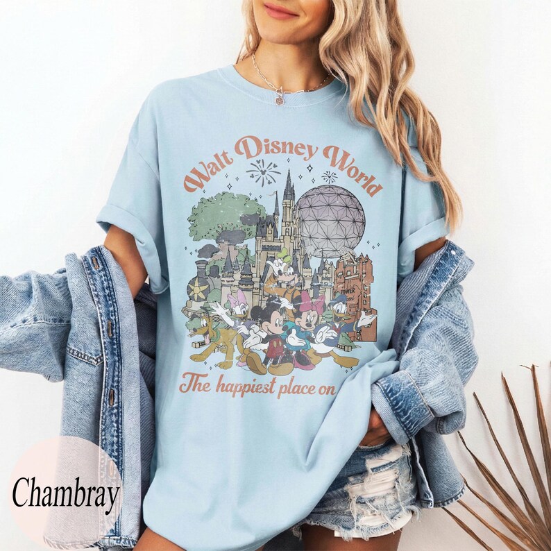 May include: Light blue t-shirt featuring a vintage-style graphic of Walt Disney World with various cartoon characters. The text on the shirt reads "Walt Disney World" and "The happiest place on". The shirt is made of a soft material.