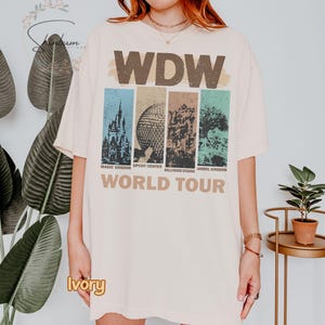 May include: Ivory colored t-shirt with a vintage graphic of the four theme parks at Walt Disney World. The graphic includes the text "WDW World Tour" and the names of each park: Magic Kingdom, Epcot Center, Hollywood Studios, and Animal Kingdom.