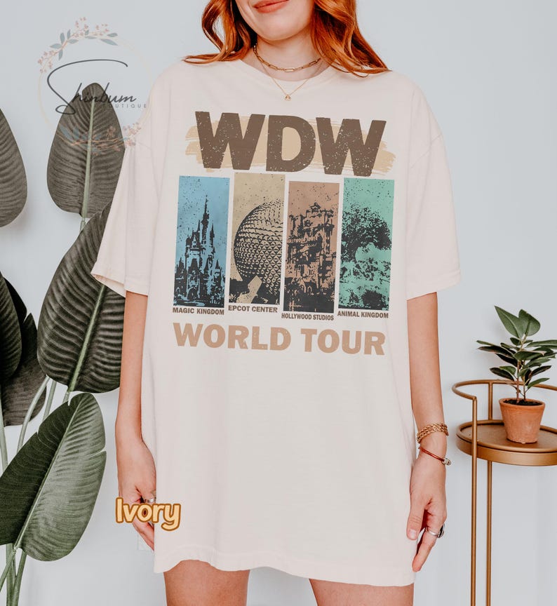 May include: Ivory colored t-shirt with a vintage graphic of the four theme parks at Walt Disney World. The graphic includes the text "WDW World Tour" and the names of each park: Magic Kingdom, Epcot Center, Hollywood Studios, and Animal Kingdom.