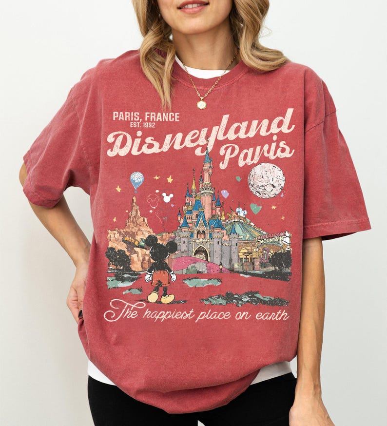 May include: Red t-shirt featuring a Disneyland Paris graphic. The design includes the Disneyland Paris logo, a castle, Mickey Mouse, and the text "The happiest place on earth." The shirt is a vintage style.
