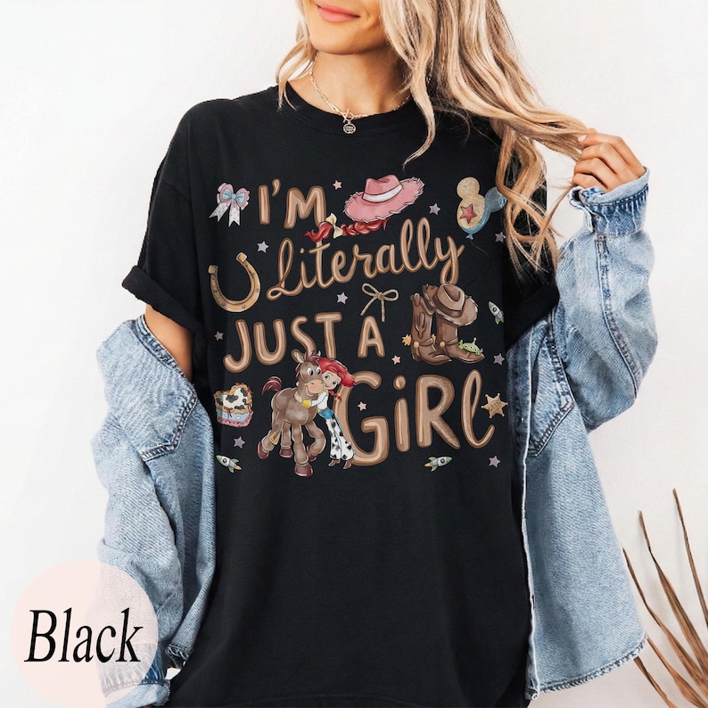 K&ouml;nnte beinhalten: Schwarzes T-Shirt mit dem Text "I'm Literally Just a Girl" und verschiedenen Cowboy-Motiven. Das Design umfasst ein Hufeisen, Cowboy-Stiefel, einen rosa Hut und ein Cartoon-Pferd.