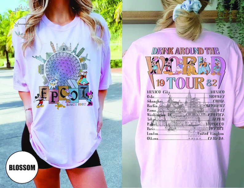 Może przedstawiać: R&oacute;żowa koszulka z grafiką World Showcase w Epcot i tekstem "Drink Around the World 19 Tour 82". Grafika zawiera Myszki Miki, Minnie Mouse, Donalda Ducka, Goofy'ego i Pluto. Na plecach koszulki znajduje się lista kraj&oacute;w i miast.