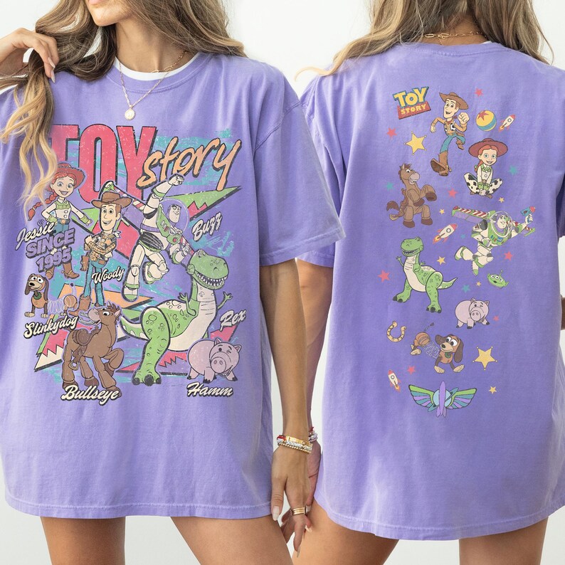 May include: A lilac-colored t-shirt featuring a Toy Story graphic. The front design includes characters like Woody, Buzz, and Rex, with the text "Toy Story" and "Since 1995." The back of the shirt also has Toy Story characters.