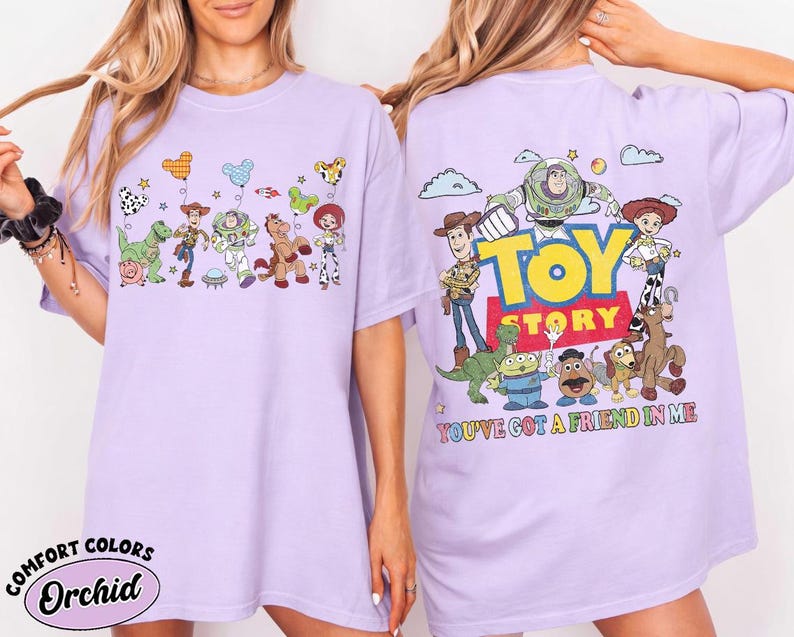 May include: A light purple t-shirt featuring Toy Story characters. The front displays a line of characters with balloons. The back features the Toy Story logo, various characters, and the text "YOU'VE GOT A FRIEND IN ME" in colorful letters.