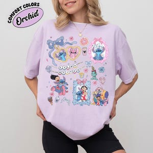 May include: A light purple t-shirt featuring various illustrations of Stitch and Angel from Lilo & Stitch. The design includes framed images, hearts, bows, and the text "Lilo & Stitch". The shirt has the text "Comfort Colors Orchid" in a circle.