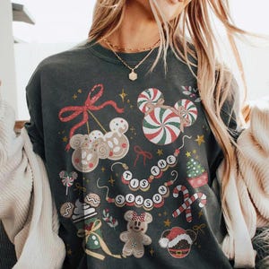 May include: Dark gray sweatshirt with a festive Christmas design. The design includes gingerbread men, candy canes, and the phrase "Tis the Season" in a circular pattern. The sweatshirt has a crew neck.