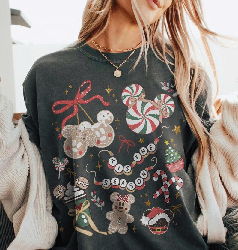 May include: Dark gray sweatshirt with a festive Christmas design. The design includes gingerbread men, candy canes, and the phrase "Tis the Season" in a circular pattern. The sweatshirt has a crew neck.