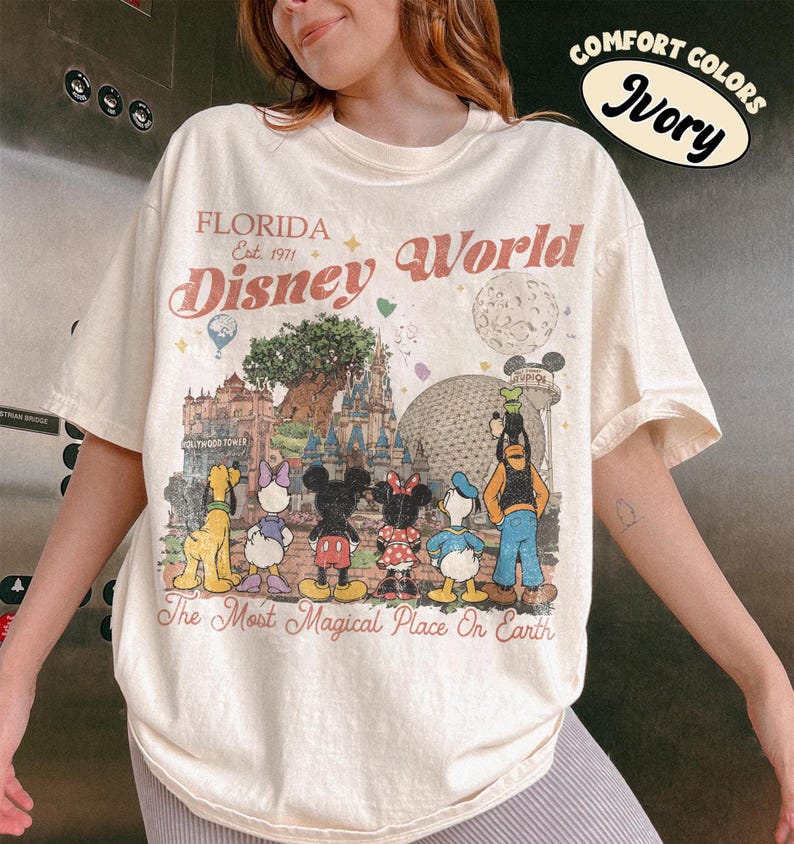 May include: Ivory t-shirt with a Disney World graphic. The design includes Disney characters, the text "FLORIDA Disney World" and "The Most Magical Place On Earth". The shirt is a comfort fit.