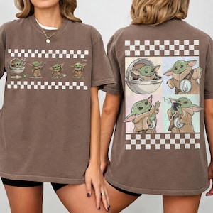 May include: Brown t-shirt featuring multiple images of a green alien character, with a checkered pattern at the top and bottom. The front of the shirt shows the character in various poses. The back of the shirt has a larger image of the character.