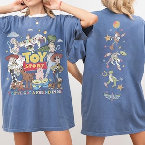 Op de afbeelding: Een blauw t-shirt met Toy Story-personages op de voor- en achterkant. De voorkant toont het Toy Story-logo, de tekst 'YOU'VE GOT A FRIEND IN ME' en diverse personages. De achterkant toont een verticale rangschikking van personages en sterren.