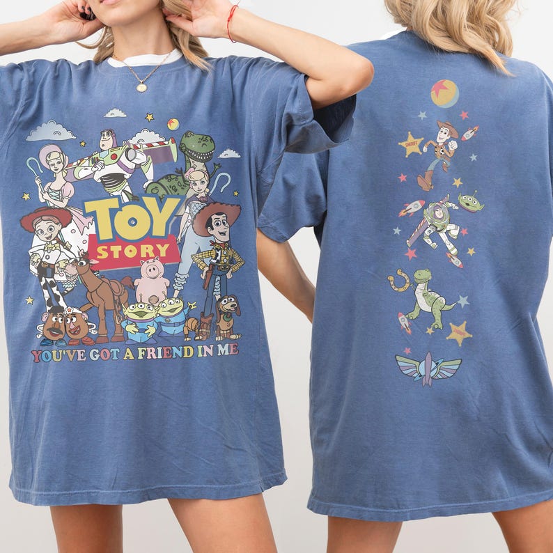 Op de afbeelding: Een blauw t-shirt met Toy Story-personages op de voor- en achterkant. De voorkant toont het Toy Story-logo, de tekst 'YOU'VE GOT A FRIEND IN ME' en diverse personages. De achterkant toont een verticale rangschikking van personages en sterren.