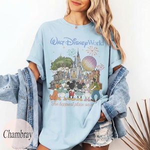 Puede incluir: Camiseta azul claro con un gr&aacute;fico colorido de personajes de Disney y el texto "Walt Disney World" y "The happiest place on earth". El dise&ntilde;o incluye un castillo, fuegos artificiales y personajes de dibujos animados.