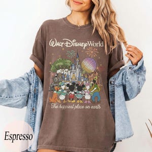 Puede incluir: Camiseta color espresso con un gr&aacute;fico de Walt Disney World, que incluye fuegos artificiales, un castillo y personajes de Disney. El texto "Walt Disney World" y "The happiest place on earth" est&aacute;n impresos.
