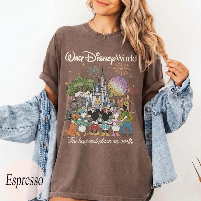 Puede incluir: Camiseta color espresso con un gr&aacute;fico de Walt Disney World, que incluye fuegos artificiales, un castillo y personajes de Disney. El texto "Walt Disney World" y "The happiest place on earth" est&aacute;n impresos.