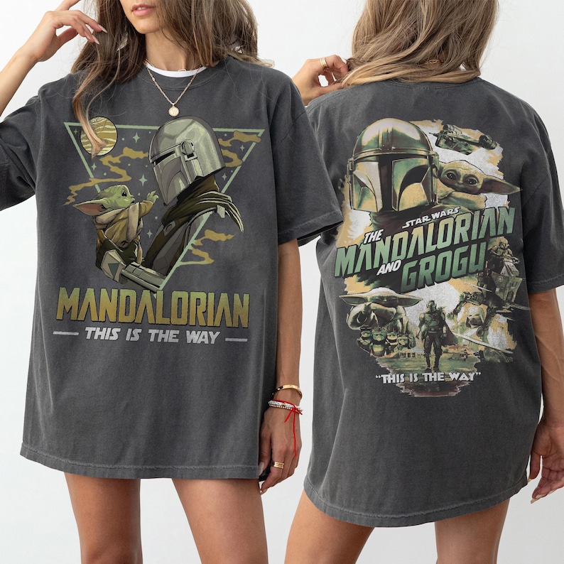 May include: Dark gray t-shirt featuring a graphic of The Mandalorian and Grogu. The front design includes the text "MANDALORIAN - THIS IS THE WAY" and a triangular graphic. The back design features the text "STAR WARS THE MANDALORIAN AND GROGU - THIS IS THE WAY".