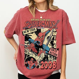 May include: Red t-shirt with a vintage Spider-Man comic book design. The graphic includes the words "BRAND NEW DAY," "SPIDER-MAN," "NEW YORK," and "2008." The superhero is shown swinging from a web. The shirt has a distressed appearance.