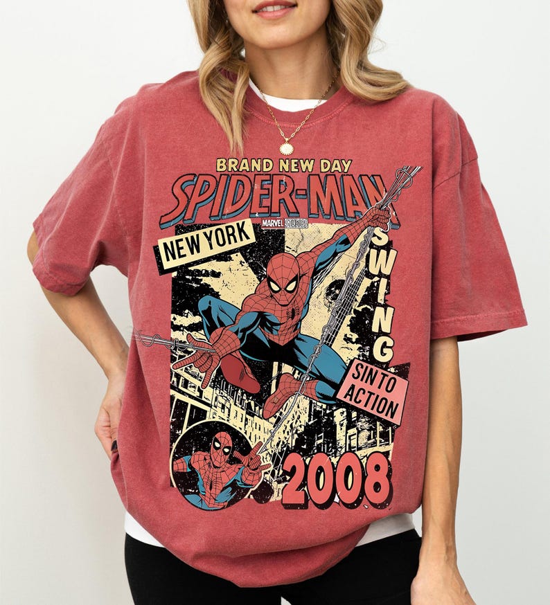 May include: Red t-shirt with a vintage Spider-Man comic book design. The graphic includes the words "BRAND NEW DAY," "SPIDER-MAN," "NEW YORK," and "2008." The superhero is shown swinging from a web. The shirt has a distressed appearance.
