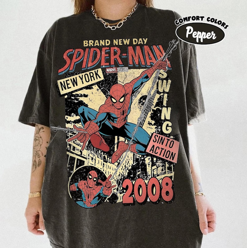 May include: Charcoal grey t-shirt with a Spider-Man graphic. The design includes the words "Brand New Day," "Spider-Man," "New York," and "2008." The superhero is shown in action, swinging. The shirt is from Comfort Colors.