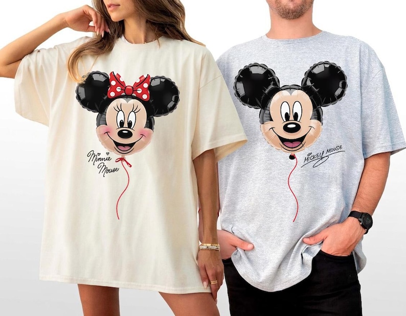 K&ouml;nnte beinhalten: Zwei &uuml;bergro&szlig;e T-Shirts, eines in Creme und eines in Grau, jeweils mit einem Cartoon-Ballon-Design. Das cremefarbene Shirt hat einen Minnie-Mouse-Ballon mit roter Schleife und dem Schriftzug "Minnie Mouse". Das graue Shirt hat einen Mickey-Mouse-Ballon.