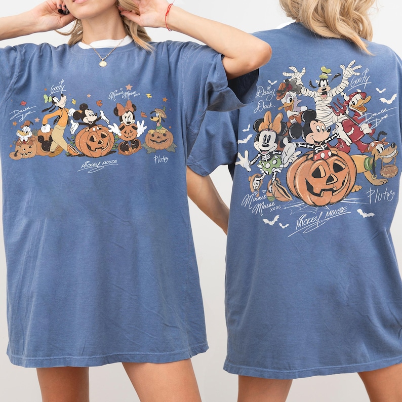 May include: Blue t-shirt featuring a Halloween-themed graphic of Disney characters, including Mickey Mouse, Minnie Mouse, and Goofy, with carved pumpkins. The design is on both the front and back of the shirt, with character signatures.