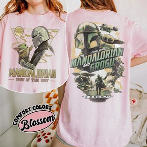 May include: Pink t-shirt featuring a graphic of The Mandalorian and Grogu. The front design includes the text "MANDALORIAN - THIS IS THE WAY" with an illustration of the characters. The back design features the text "STAR WARS THE MANDALORIAN AND GROGU" and other characters.