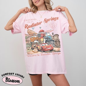 以下が含まれることがあります： ライトピンクのTシャツ。映画「カーズ」のキャラクター、ライトニング・マックィーンなどのグラフィックが描かれています。Tシャツには「California, Radiator Springs, Welcome to Radiator Springs」という文字がヴィンテージスタイルで書かれています。Comfort Colors Blossomの生地で作られています。