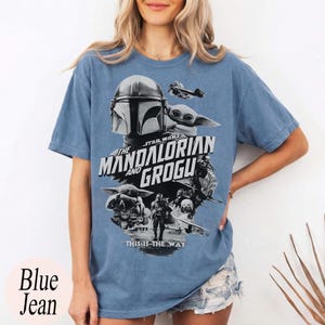 Op de afbeelding: Blauw spijkerbroekkleurig T-shirt met een afbeelding uit de Star Wars-serie, "The Mandalorian and Grogu". Het ontwerp bevat afbeeldingen van de Mandalorian, Grogu en andere personages, met de zin "This is the Way".