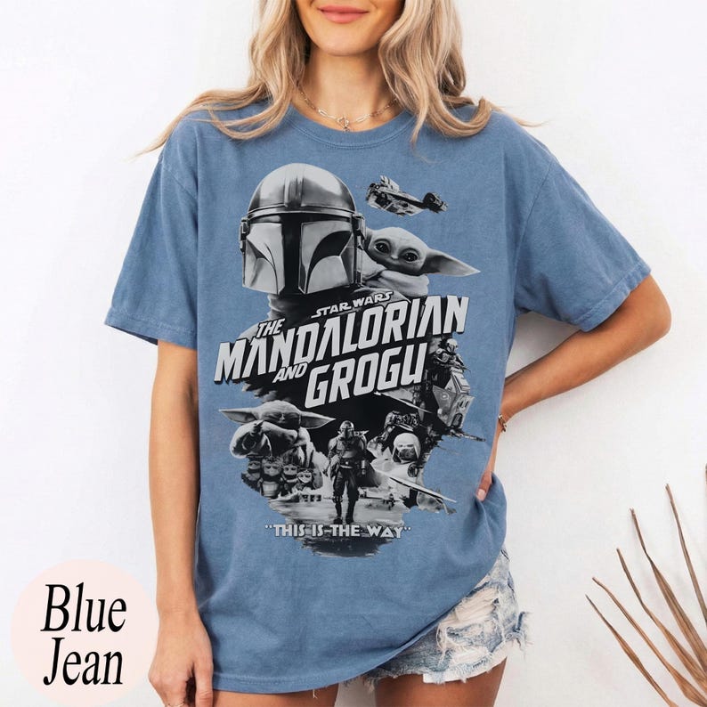 Op de afbeelding: Blauw spijkerbroekkleurig T-shirt met een afbeelding uit de Star Wars-serie, "The Mandalorian and Grogu". Het ontwerp bevat afbeeldingen van de Mandalorian, Grogu en andere personages, met de zin "This is the Way".