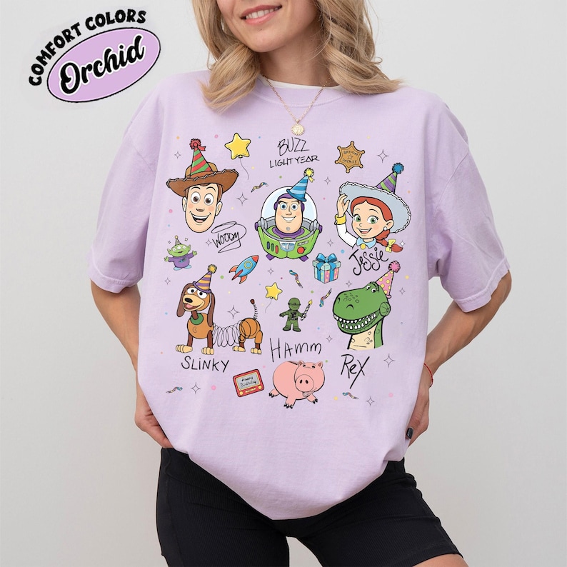 Pu&ograve; includere: Una maglietta lilla con personaggi dei cartoni animati del film Toy Story. La maglietta presenta Woody, Buzz Lightyear, Jessie, Slinky, Hamm e Rex. Il testo "COMFORT COLORS" e "Orchid" &egrave; in un cerchio in alto a sinistra.