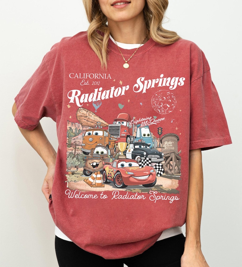 以下が含まれることがあります： 映画「カーズ」のキャラクターのグラフィックが特徴の赤いTシャツ。テキストには「California Est. 2012 Radiator Springs」と「Welcome to Radiator Springs」が含まれています。ヴィンテージ感のあるデザインです。
