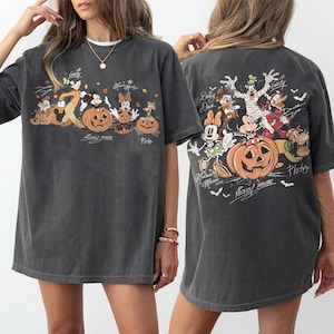 May include: Dark gray t-shirt featuring a Halloween-themed graphic with Disney characters and pumpkins. The front of the shirt displays Mickey Mouse, Minnie Mouse, Goofy, and Pluto. The back of the shirt shows the same characters in Halloween costumes.