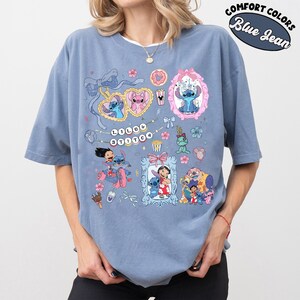 May include: Blue jean-colored t-shirt featuring multiple cartoon images of Stitch. The shirt has a crew neck and short sleeves. The graphic includes the text "Lilo & Stitch" and other cartoon elements. The shirt is labeled "Comfort Colors".