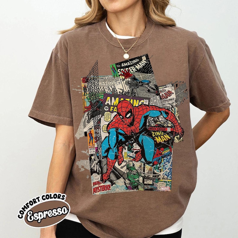 Pode incluir: Camiseta marrom com um design de colagem de quadrinhos do Homem-Aranha. O design inclui as palavras "The Amazing Spider-Man" e "Zing Man". A camiseta &eacute; da marca "Comfort Colors".