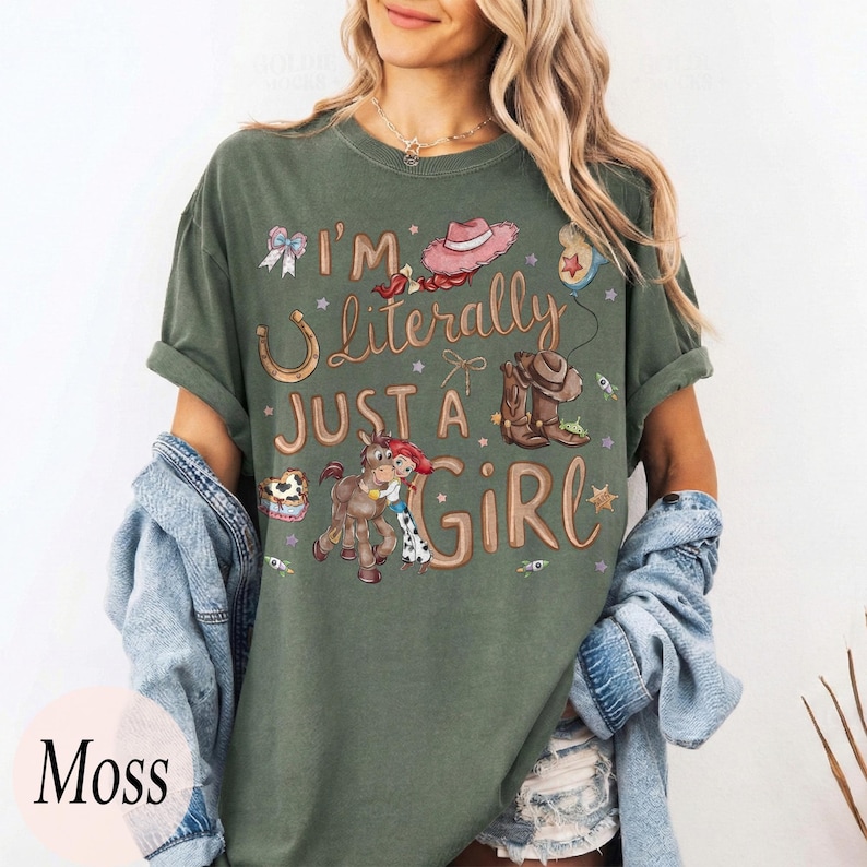 K&ouml;nnte beinhalten: Moosgr&uuml;nes T-Shirt mit dem Text "I'm Literally Just a Girl" und einer Grafik eines Hufeisens, Cowboyhuts, Stiefel und eines Cartoon-Pferdes und Cowgirls. Das Shirt hat kurze &Auml;rmel und eine lockere Passform.