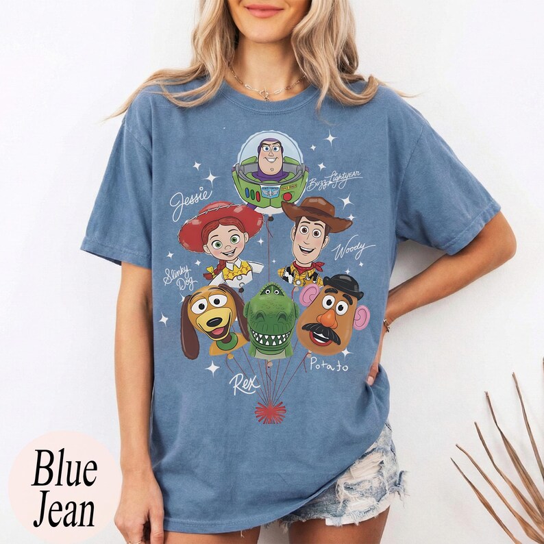 Puede incluir: Camiseta azul vaquero con un gr&aacute;fico de personajes de Toy Story como globos. Los personajes incluyen a Buzz Lightyear, Woody, Jessie, Slinky Dog, Rex y Mr. Potato Head. El texto "Blue Jean" est&aacute; impreso en la parte inferior izquierda.