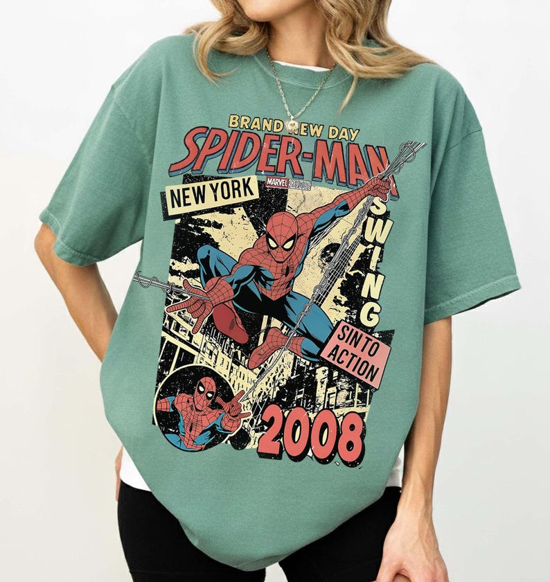 May include: Green t-shirt with a Spider-Man comic book design. The graphic includes the words "Brand New Day", "Spider-Man", "New York", and "Swing Into Action". The design also features the year "2008" and an illustration of Spider-Man.