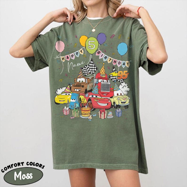 K&ouml;nnte beinhalten: Moosgr&uuml;nes T-Shirt mit einer farbenfrohen Grafik von Zeichentrickautos, Luftballons und dem Text "HAPPY BIRTHDAY" mit einem "5" Luftballon. Das Shirt enth&auml;lt auch die Texte "Name" und "95". Das Shirt ist von der Marke Comfort Colors.