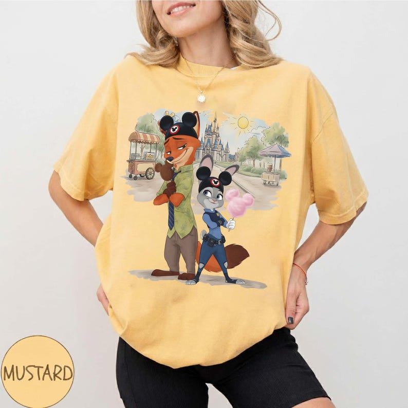 Puede incluir: Camiseta amarilla mostaza con una ilustraci&oacute;n de dibujos animados de Nick Wilde y Judy Hopps de Zootopia, con orejas de Mickey Mouse. Los personajes est&aacute;n frente a una escena de parque con un castillo y algod&oacute;n de az&uacute;car.