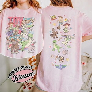 May include: Pink t-shirt featuring a colorful graphic of Toy Story characters, including Woody, Buzz Lightyear, and Rex. The front of the shirt displays the words "Toy Story" and "Jessie Since 1995". The back of the shirt has additional character graphics.