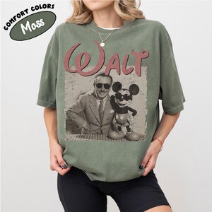 May include: Moss green t-shirt featuring a vintage graphic of Walt Disney and Mickey Mouse. The word "Walt" is printed in a faded red font above the image. The shirt has a relaxed fit and short sleeves.