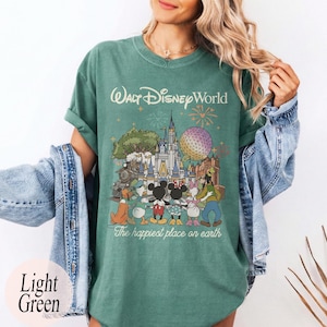 Puede incluir: Camiseta verde claro con un gr&aacute;fico de personajes y lugares emblem&aacute;ticos de Walt Disney World. El texto "Walt Disney World" y "The happiest place on earth" est&aacute;n impresos en la camiseta. La camiseta es de color verde claro.