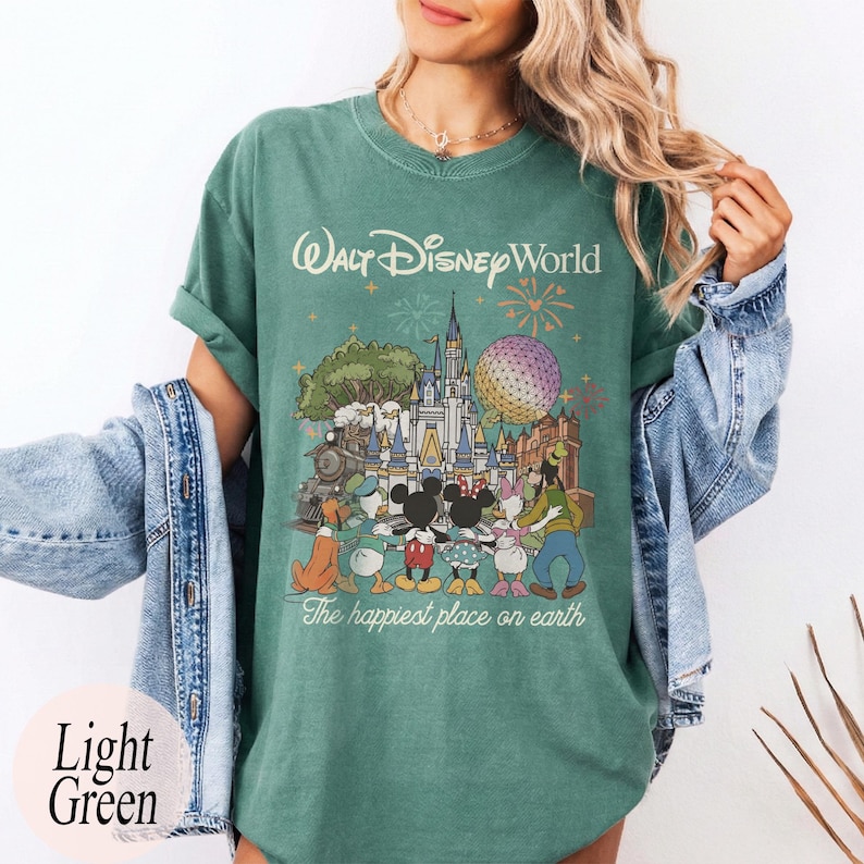 Puede incluir: Camiseta verde claro con un gr&aacute;fico de personajes y lugares emblem&aacute;ticos de Walt Disney World. El texto "Walt Disney World" y "The happiest place on earth" est&aacute;n impresos en la camiseta. La camiseta es de color verde claro.