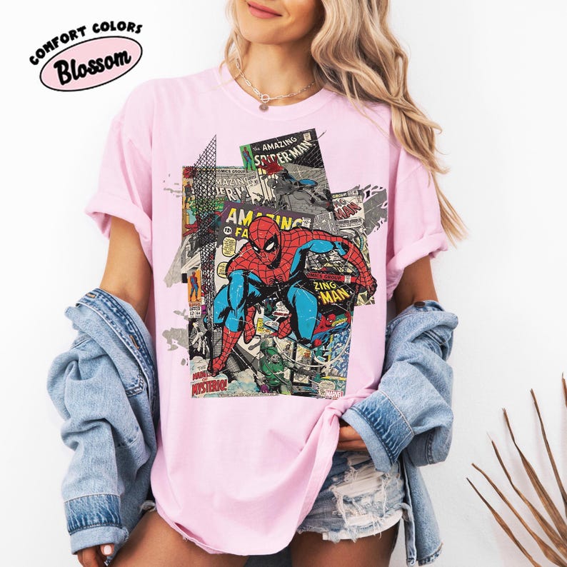 Pode incluir: T-shirt rosa claro com um gr&aacute;fico de banda desenhada do Homem-Aranha. O design incorpora pain&eacute;is de banda desenhada e elementos de texto. A t-shirt tem o texto "Comfort Colors Blossom" num oval rosa.